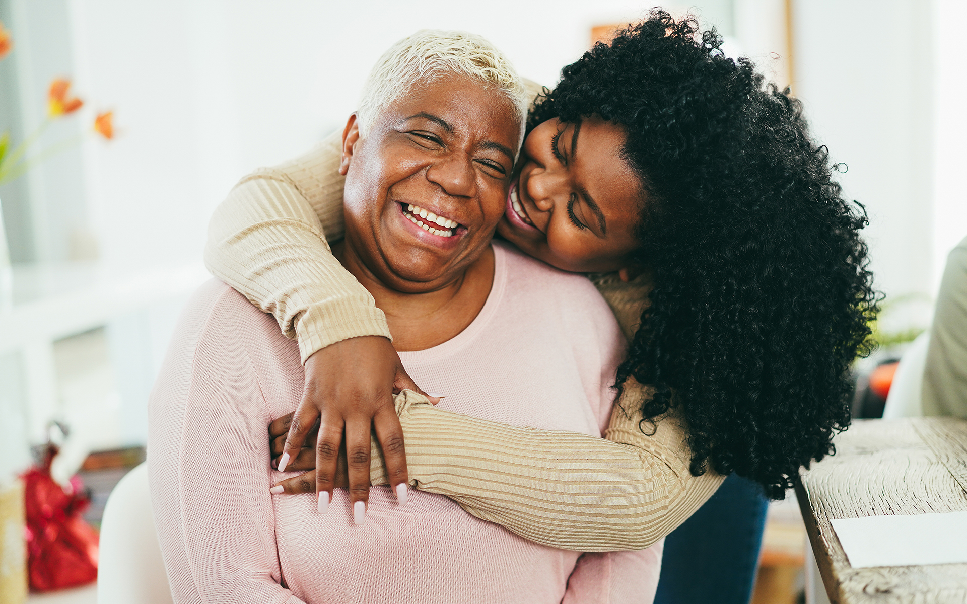 A mother and adult daughter sharing a joyful embrace at home