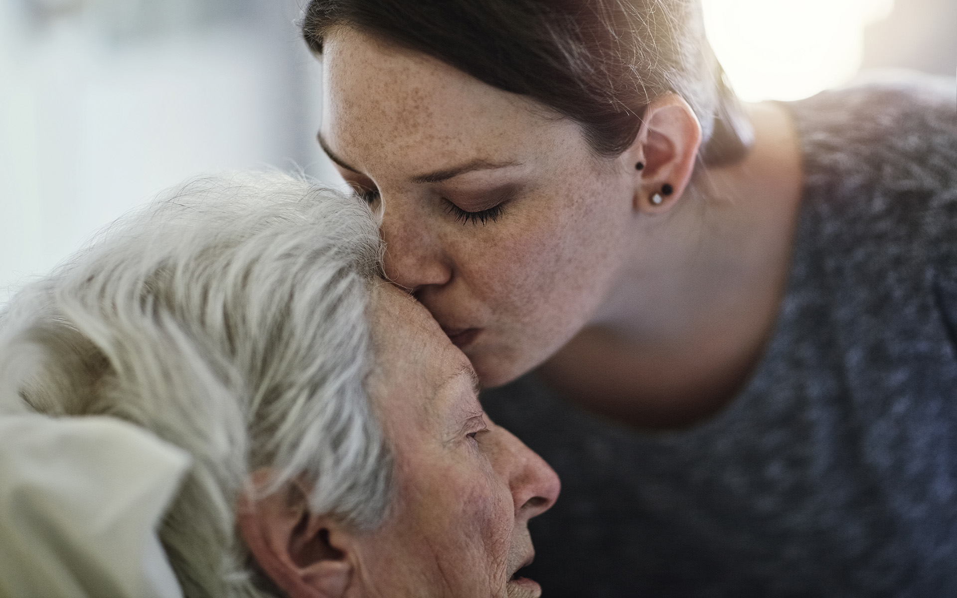 An adult daughter gently kissing her mother at home